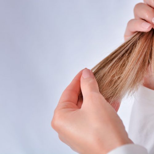 Blonde girl holding hair in hand and looking new colored hairstyle. The girl admires her hairstyle. Cares about healthy and clean hair. Beauty salon concept. Close up, selective focus